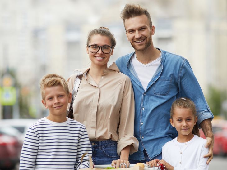 Család bevásárlókocsival a szupermarket parkolója előtt