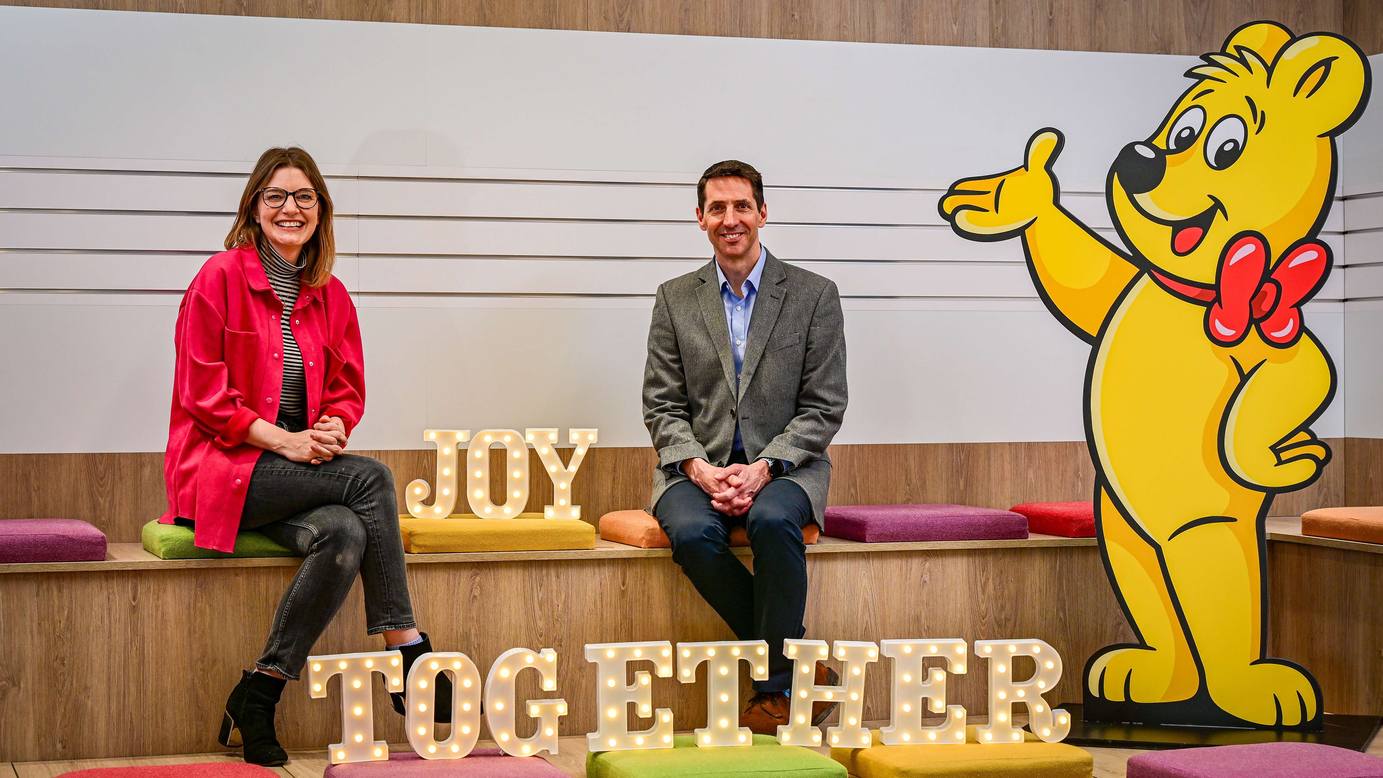 HARIBO UK Managing Director, Jon Hughes and the Founder and CEO of The Together Project pose with a light up sign saying "Joy Together"