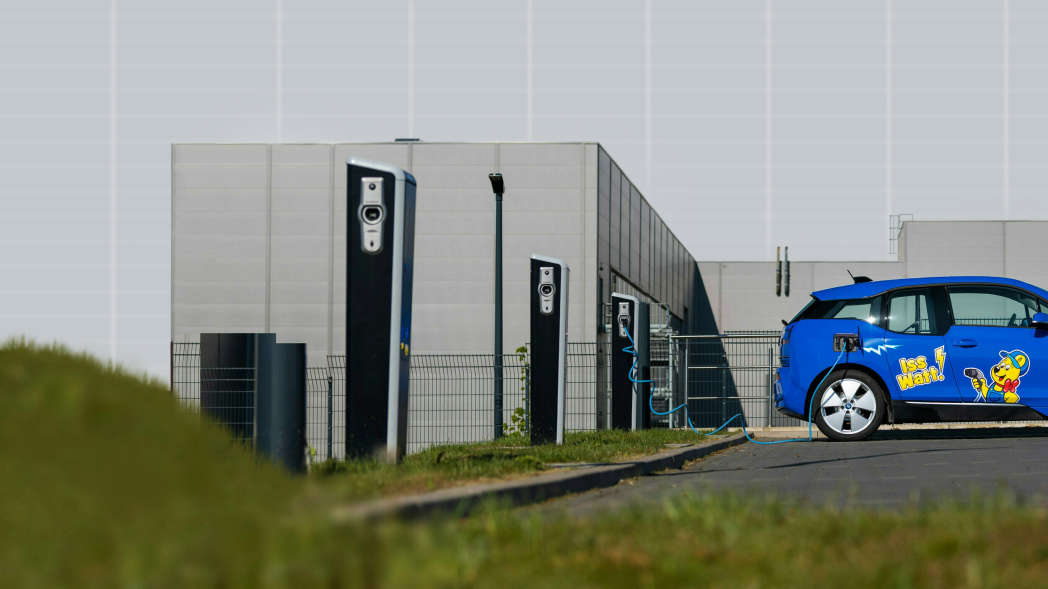 Μπλε ηλεκτρικό όχημα με επιγραφή HARIBO μπροστά από έναν σταθμό φόρτισης