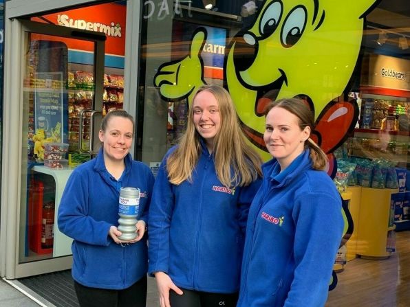 Three women with charity tin in front of HARIBO store