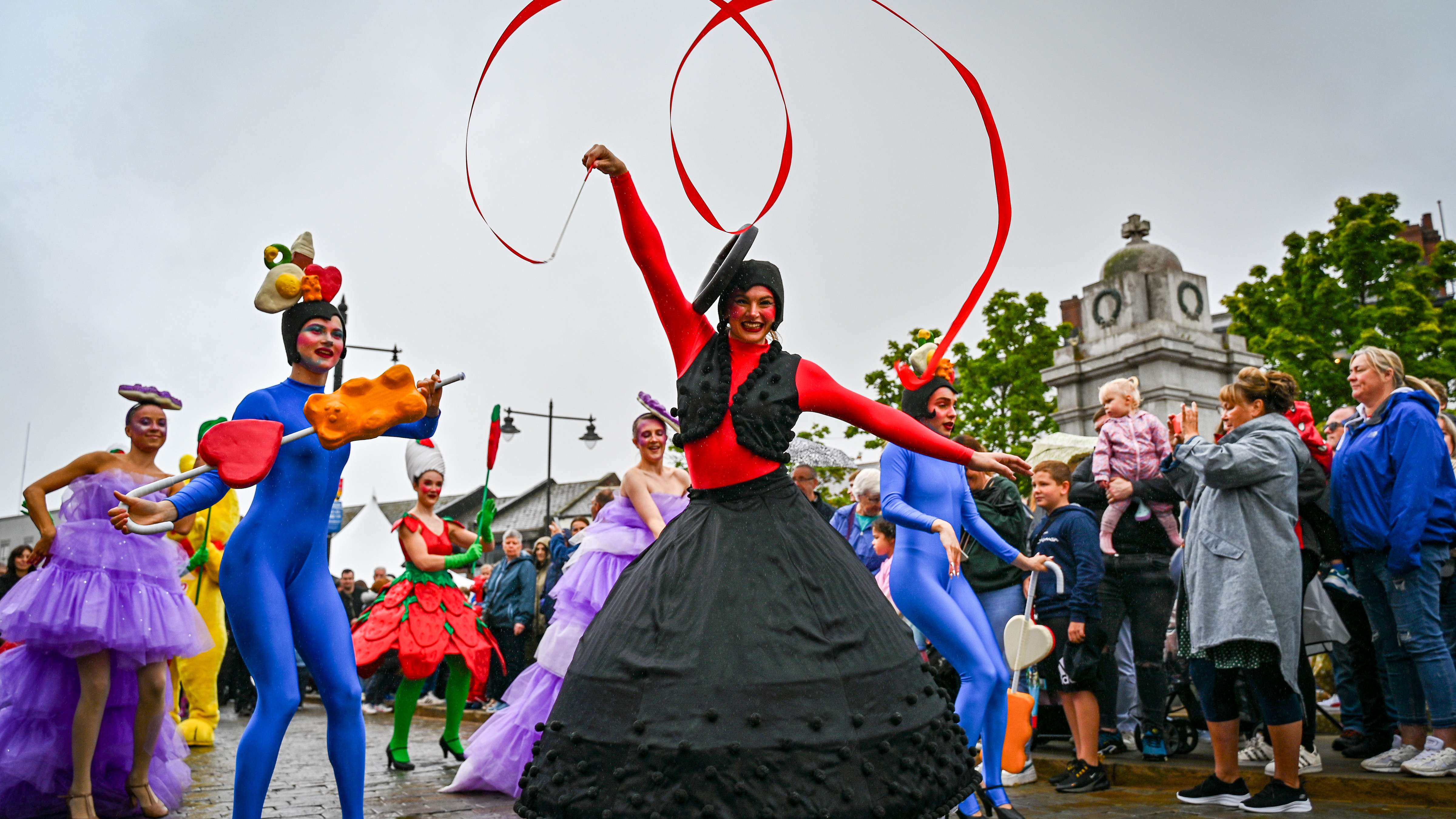Dancer in red and black dress with Pontefract Cake head piece twirls a ribbon during performance.