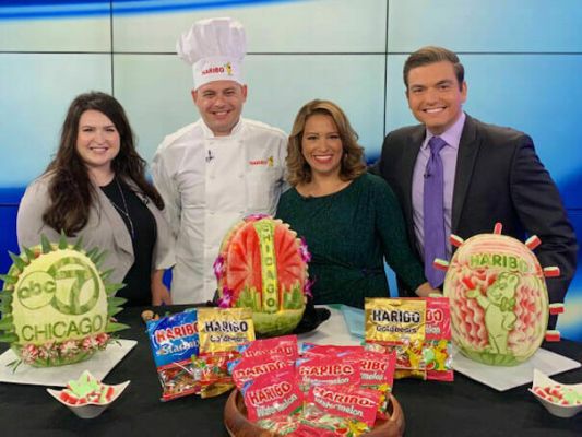 Head of Corporate Communications, Lauren Triffler, Chef and newscasters pose with watermelon sculptures in ABC7 Chicago Studio