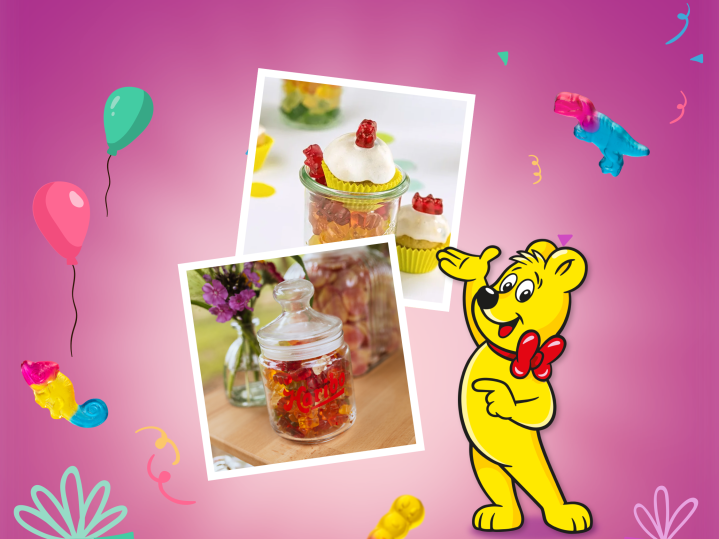 A colorful website header for HARIBO's guide to the best candy bar ideas for any celebration. The pink gradient background features balloons, confetti, and floating gummy bears. Two Polaroid-style photos showcase creative candy table ideas — one displaying cupcakes topped with gummy bears in decorative jars as a charming diy candy bar setup, and the other showing a glass jar filled with HARIBO gummy bears alongside fresh flowers for a rustic candy bar wedding or party look. The HARIBO Goldbear stands beside the photos.