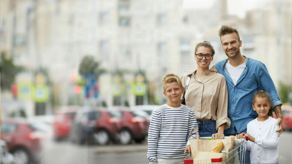 Familie steht mit Einkaufswagen vor Supermarkt Parkplatz