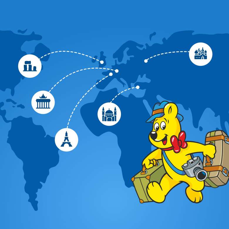 Goldbear with travel suitcases on a map showing well known sights: eifel tower, berlin gate, jesus statue brazil