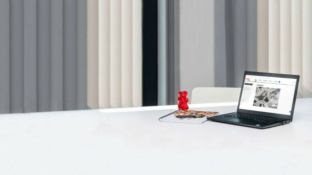사무실 책상 위에 커다란 빨간 골드베어와 함께 놓여 있는 노트북