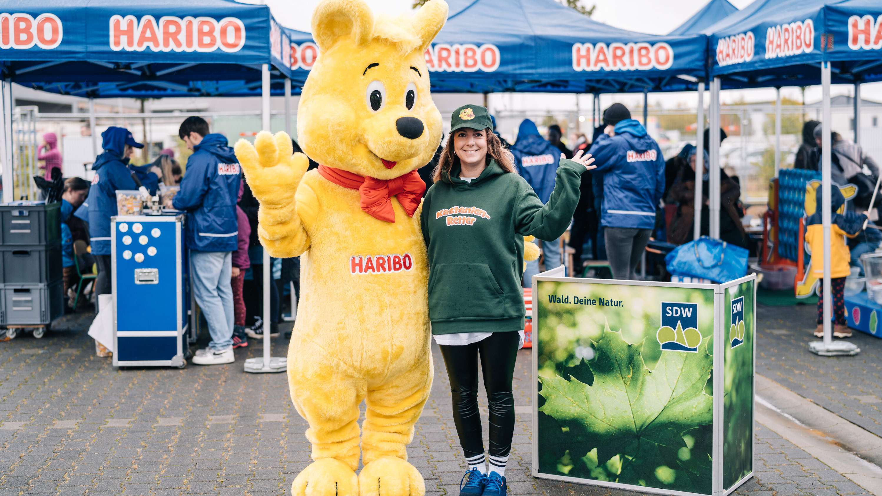 Eine HARIBO-Mitarbeiterin und der Goldbären Walking-Act informieren über die Kastanienrettung.