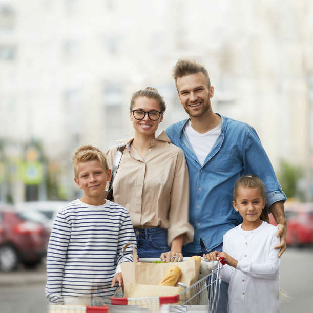 Familie steht mit Einkaufswagen vor Supermarkt Parkplatz