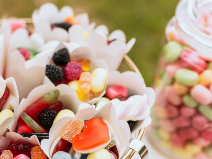 Nahaufnahme von Papiertüten für eine Candy-Bar, gefüllt mit unterschiedlichen HARIBO-Süßigkeiten. Im Hintergrund ist ein Glasbehälter mit MAOAM Krachern zu sehen.