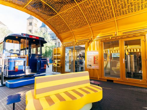 Das HARIBO Pop-up-Museum von innen mit dem Eingang zum Ausstellungsbus, der Goldbären-Produktionsmaschine und einem Sofa in Goldbären-Form.