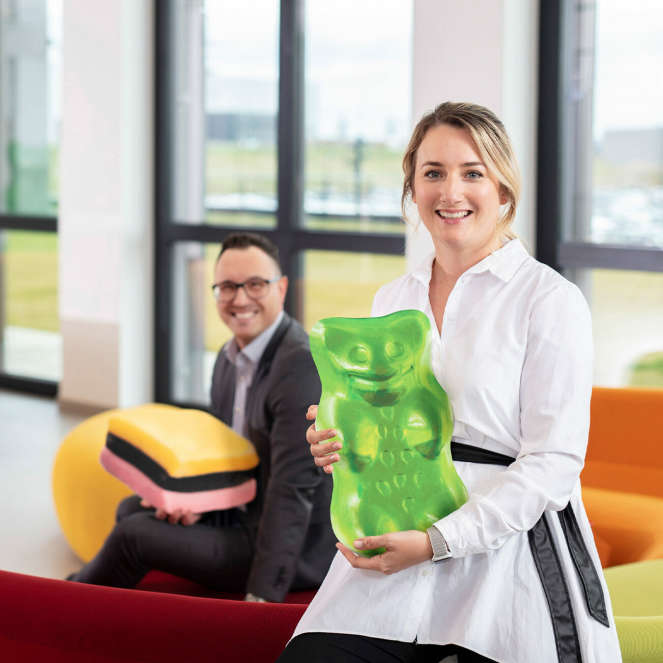 Two employees holding oversized products, placed in a headquarter lounge.