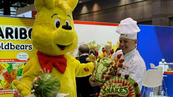 Goldbear and chef with watermelon sculptures at Sweets and Snacks Expo