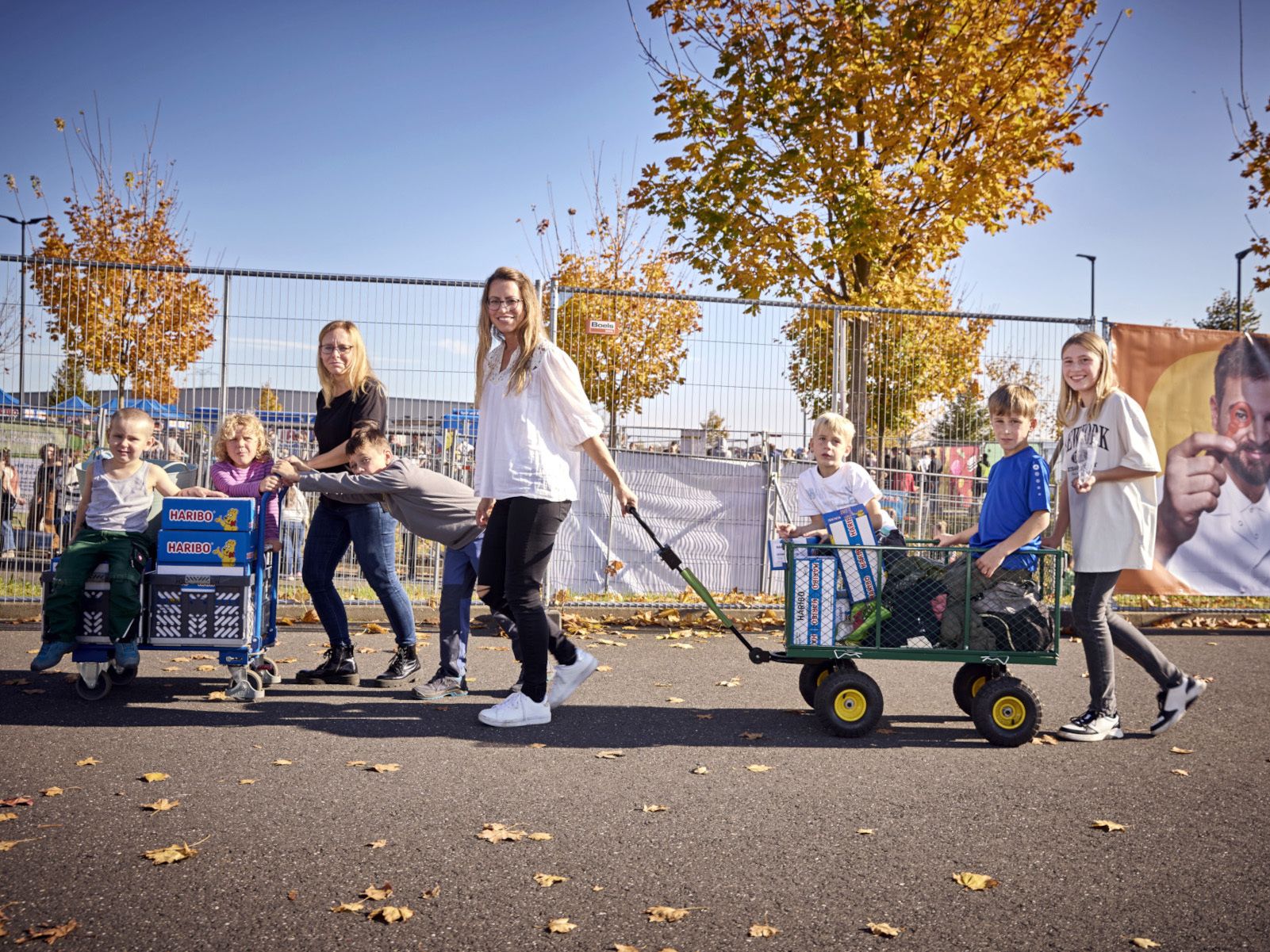 Zwei Mütter und mehrere Kinder ziehen Bollerwagen voller HARIBO-Produkte.