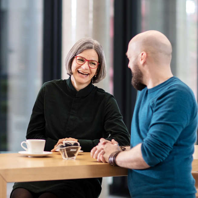 Zwei Mitarbeiter unterhalten sich in der Cafeteria und lachen