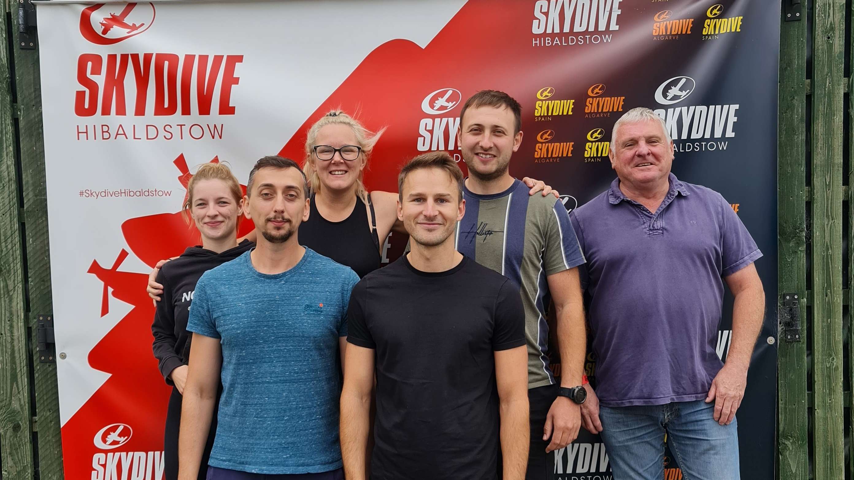 HARIBO colleagues on the ground pose in front of a banner before their charity skydive.