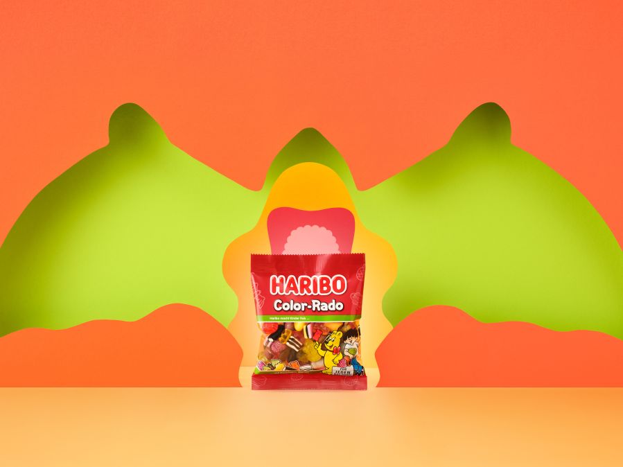 HARIBO Color-Rado Beutel mit verschiedenen Schatten der Produktstücke vor einem orangenen Hintergrund